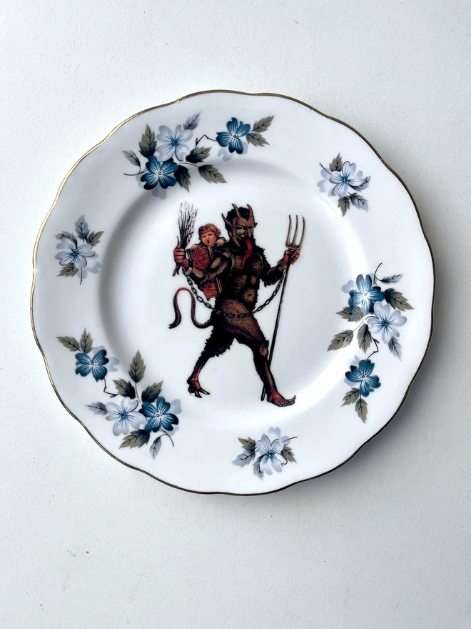 a naughty Christmas Krampus stealing a child, the image is victorian and is printed directly onto an ornate vintage plate