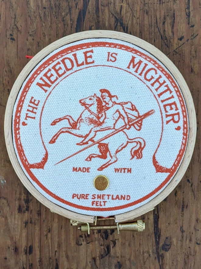 Orange coloured 'the needle is mightier' embroidery hoop needle book depicting a soldier on horse back with a needle as a sword