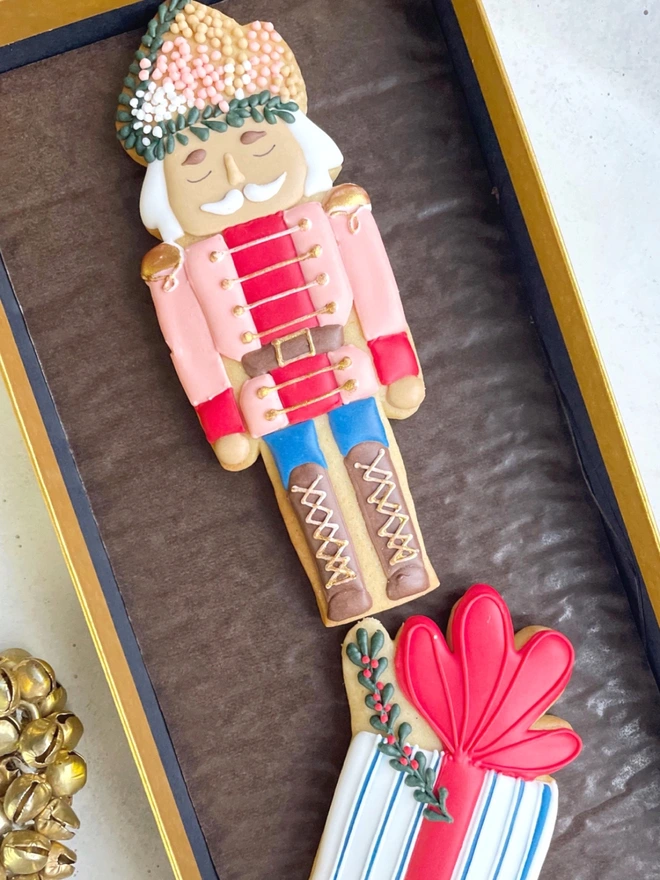 Hand-iced Christmas biscuits featuring a Nutcracker and a present in a festive gift box, available in Vanilla or Gingerbread flavour.
