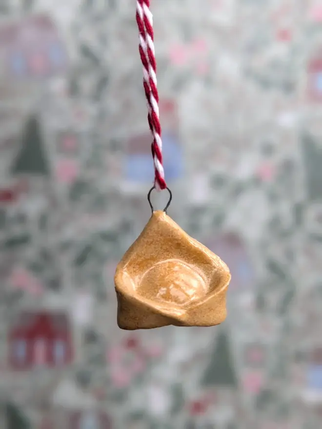 ceramic tortellini christmas decoration. a small pasta ornament hanging from red and white thread.