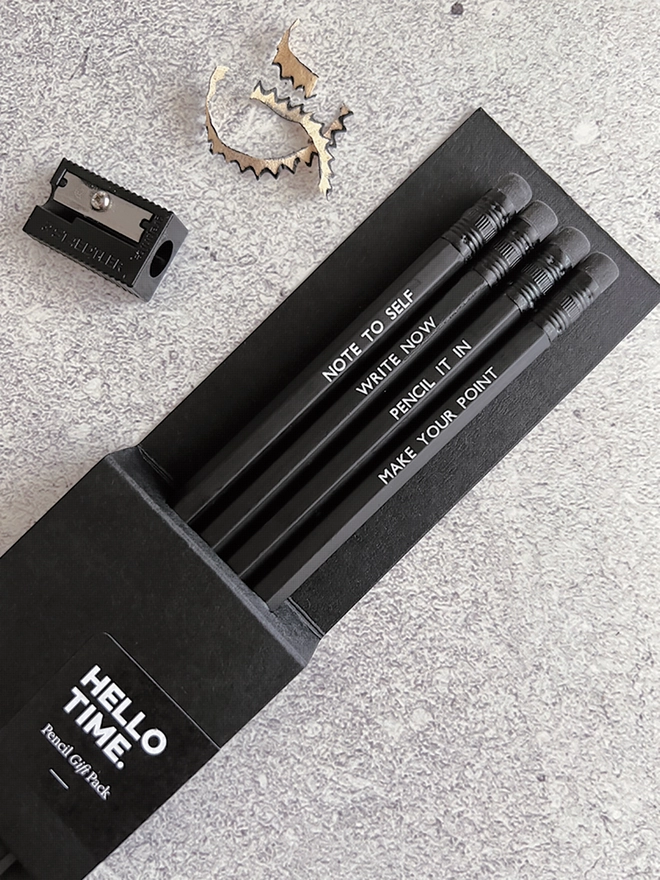 Four black pencils each with a different quote on in a card sleeve, pencil sharpener