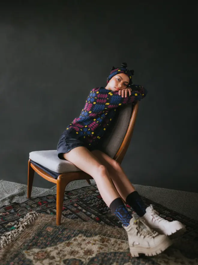 Model wearing pieces from MABLI's 'Carthen' collection, featuring the Carthen Jumper in the vibrant 'Fireworks' colour-way. The design showcases bold, colourful patterns inspired by traditional Welsh blanket tapestry.