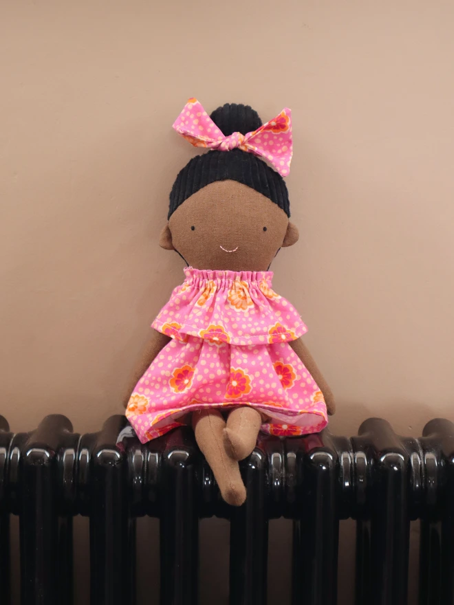 African-inspired handmade cloth doll with deep brown fabric skin, wearing a pink floral dress and matching bow