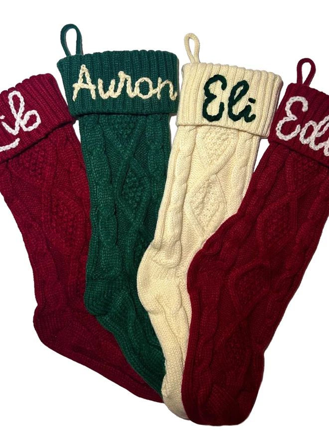 Knitted Personalised Christmas Stockings, a collection of Christmas stockings laid out on a white surface. They are each personalised. 
