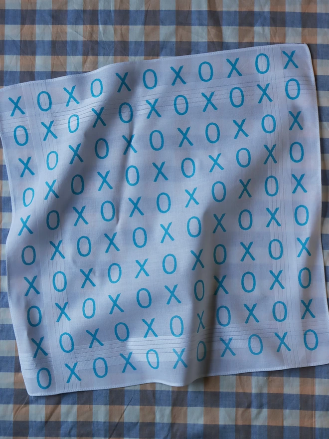 A Mr.PS Hugs and Kisses handkerchief printed in aqua on a blue gingham tablecloth
