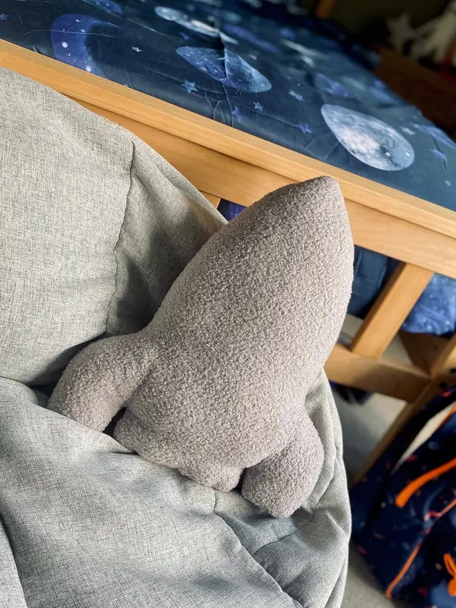 boucle rocket pillow. a grey rocket cushion on a bed.