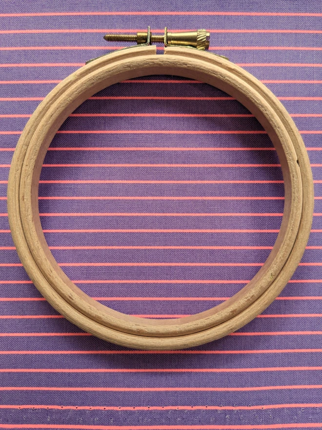 A wooden embroidery hoop lying on a stripy purple fabric