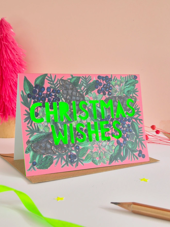 Pine Cone and blue berry illustration card with Christmas Wishes in paper cut text and a neon green backing paper 