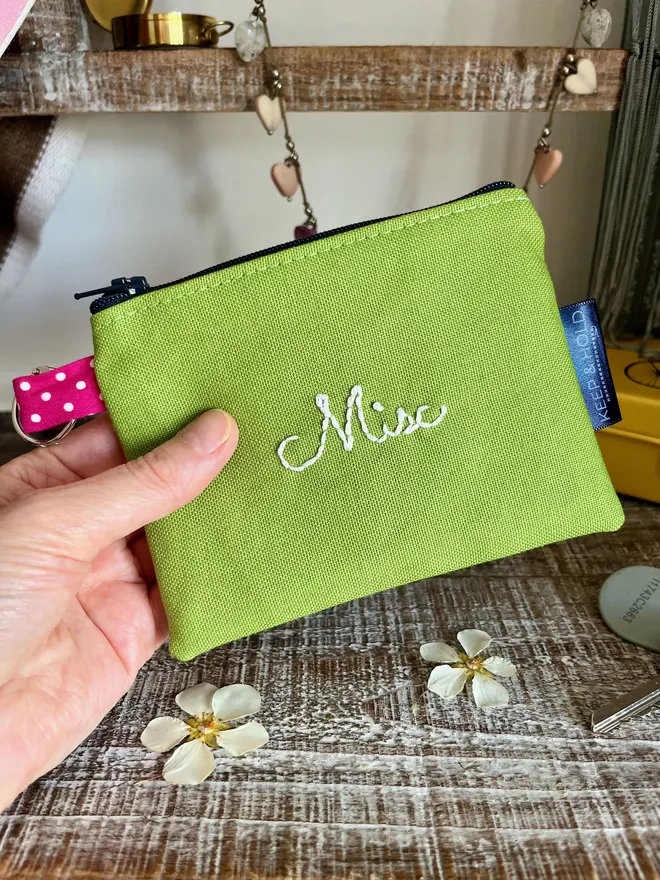 Small green zip coin purse with silver keyring & embroidered in white thread with 'Misc'.