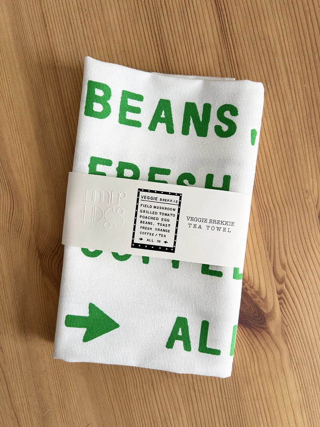 Mr.PS Veggie Brekkie Tea Towel folded on a pine table