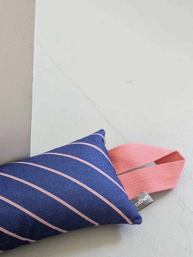 Draught Excluder, a colourful patterned draught excluder sitting on the floor by a white door. 