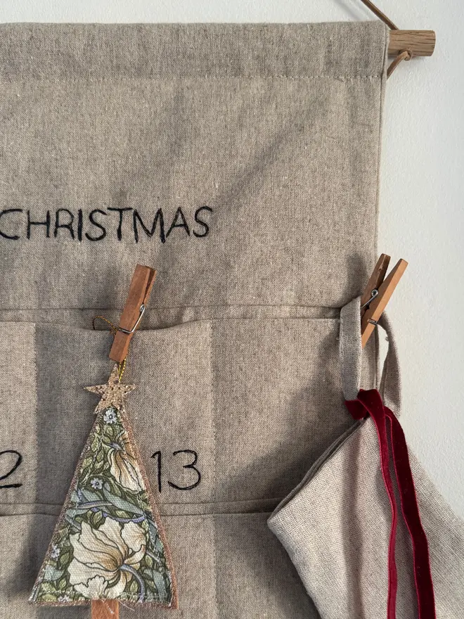 Linen Embroidered Advent Calendar. Close up of dowel and cord and a few decorations 