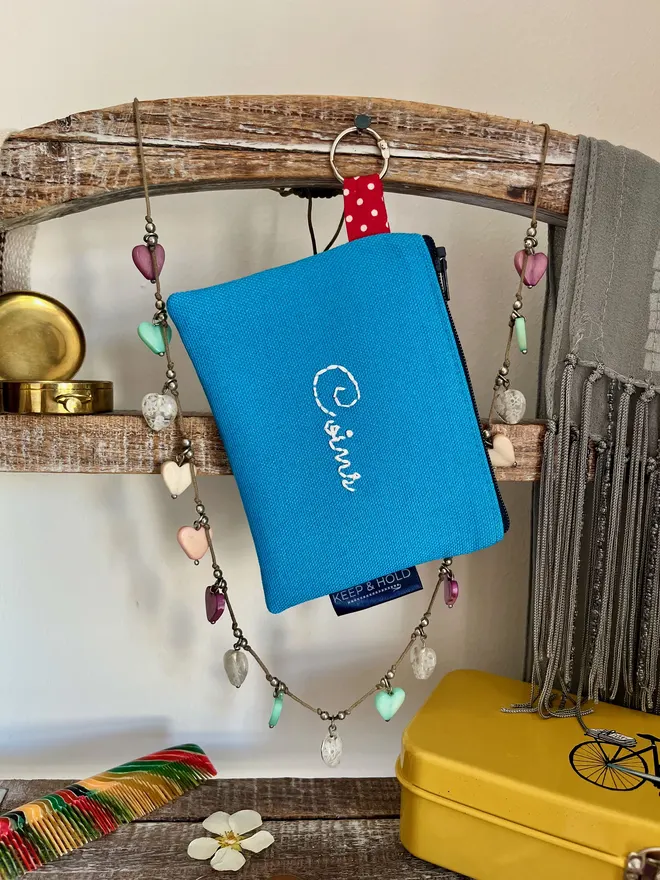 Blue coin purse hanging by attached silver key ring. 'Coins' embroidered in white on the front.