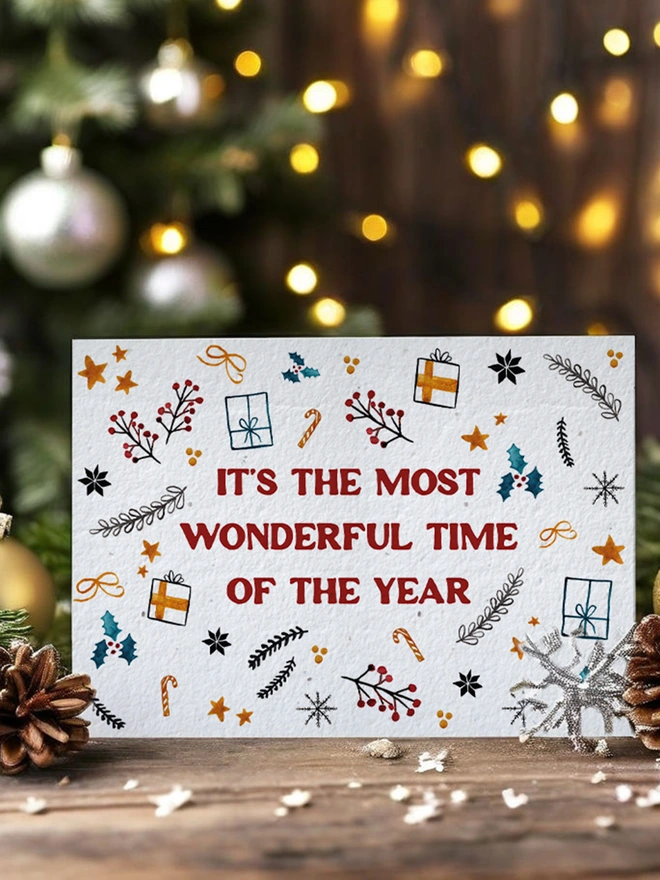 Christmas card with twinkly lights, greenery and pine cones. The Christmas Card features Christmas illustrations with 'Its the most wonderful time of the year' on