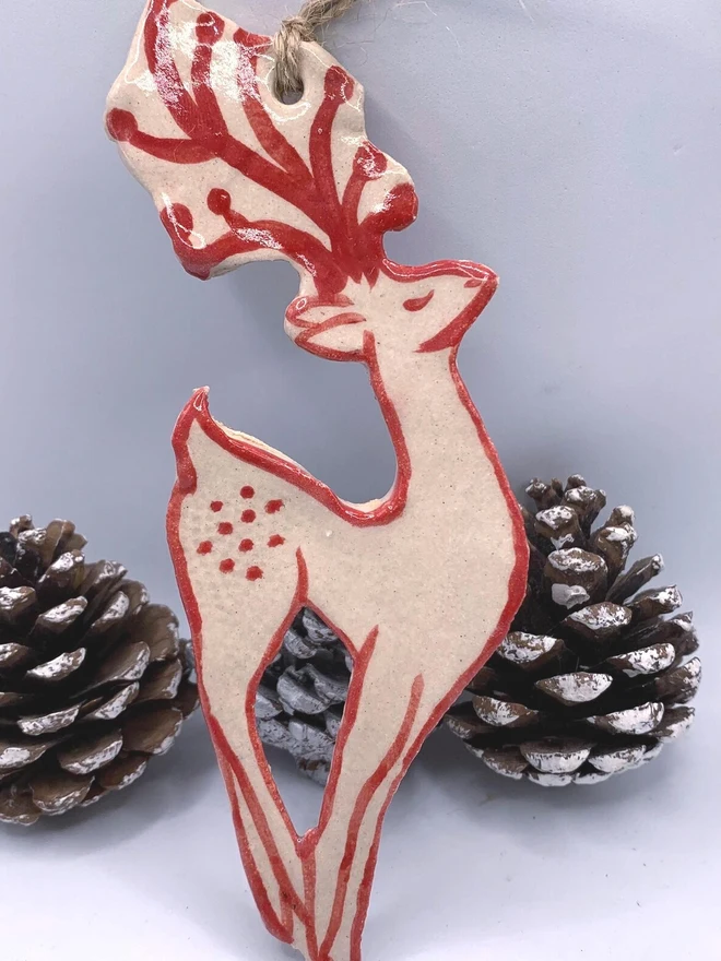 Handmade Ceramic Reindeer Ornament Scandinavian Folk Decor, a colourful reindeer decoration sitting on a plain surface joined by some acorns. 