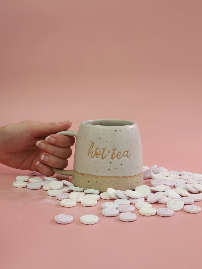 white handmade mug with saying hot tea on the front being picked up 