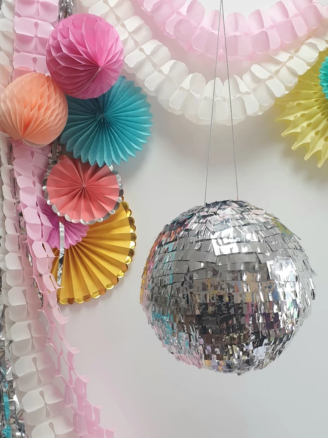 Silver glitter ball pinata surrounded by paper decorations