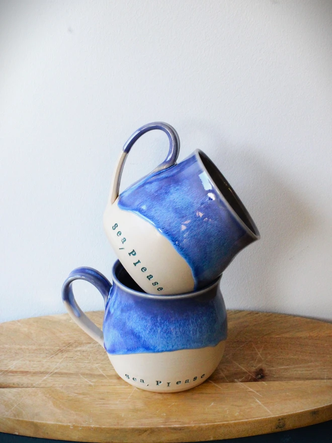 Pile of two Blue and natural ceramic mugs with 'Sea Please' stamped