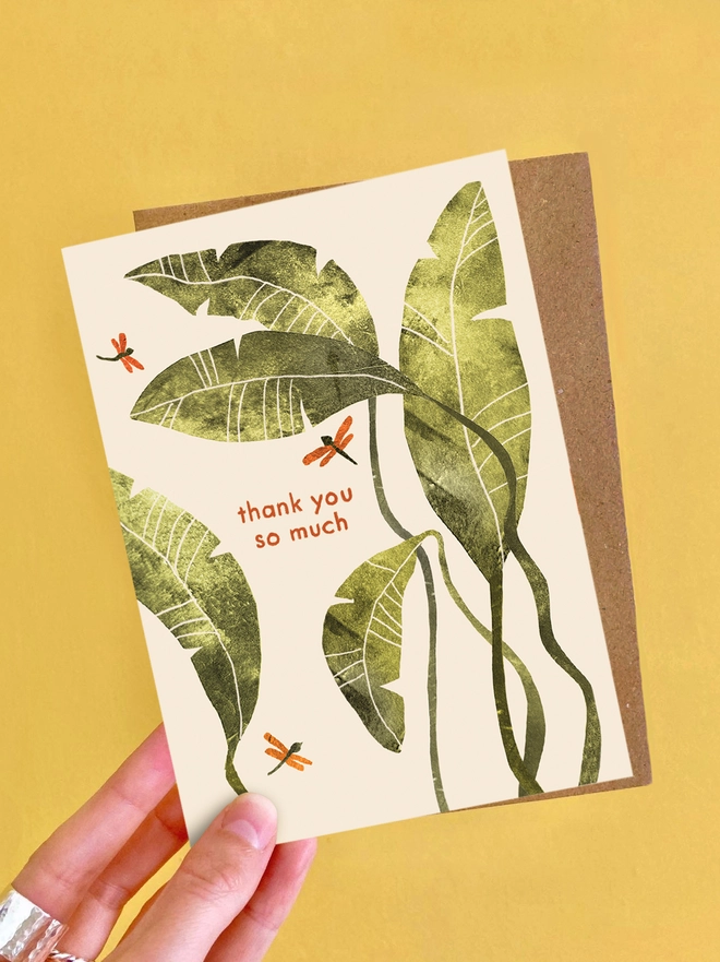 An illustrated greeting card by Emily Nash Illustration, featuring a palm leaf design. The collage illustration is textural and primarily green in colour. The card features the words 'thank you so much'.