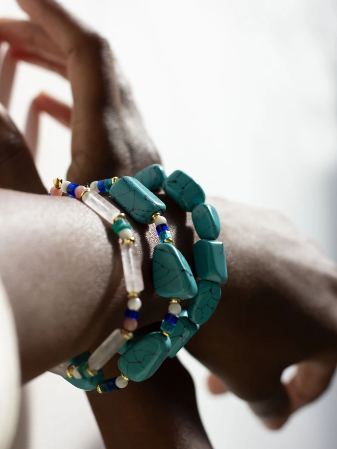 Hand wearing multiple turquoise bracelets on a neutral background