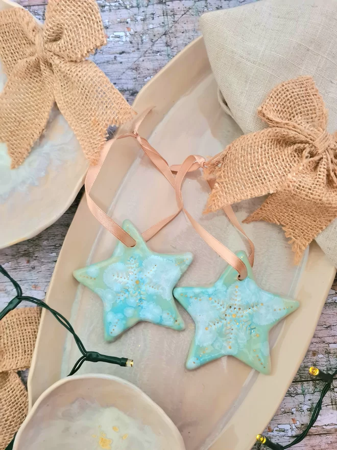 Star Christmas decorations, ceramic decorations, dream catcher, christmas star, pottery, Jenny Hopps Pottery, J.H Pottery, J.Hopps Pottery, Clay star, gift, christmas tree, blue with white and cream with gold details, on a light gold ribbon, photographed on a branch with Christmas lights