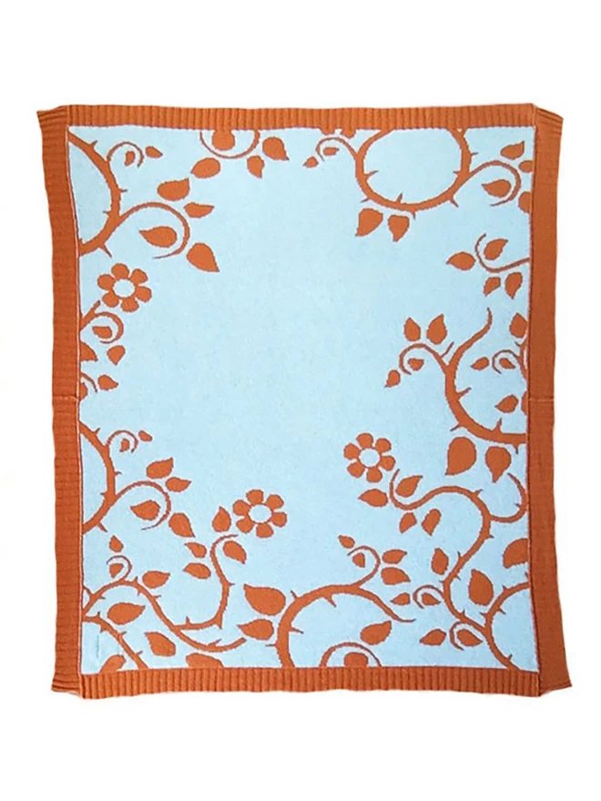 Product shot of the reverse colourway of the rust briar rose junior blanket, muted blue background with rust orange trailing flower and thorn design.