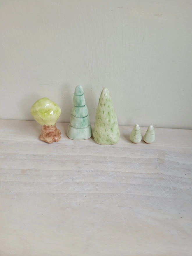 a row of assorted green ceramic trees on a light wooden surface