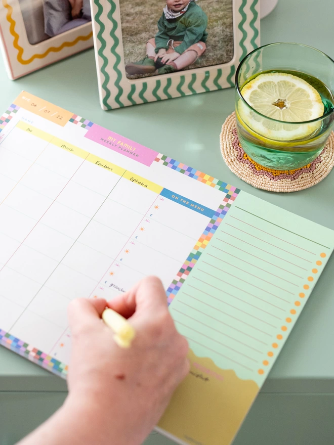 Writing in the Raspberry Blossom Family Weekly Planner, there sare four spaces for each family member and even a space for writing out the meal plan for each day