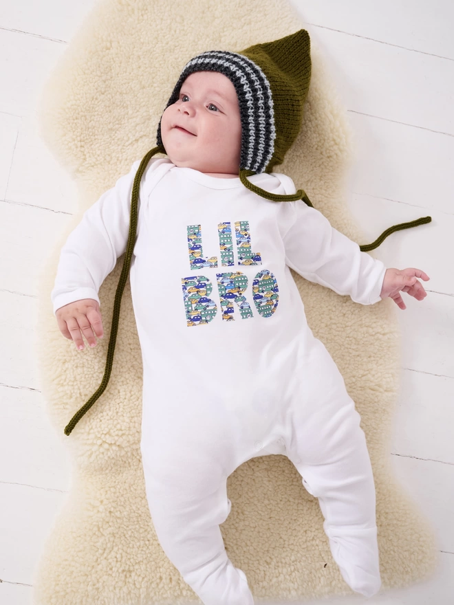 Lil Bro appliquéd on a white cotton baby romper in a vintage cars and busses Liberty print. worn by a happy baby.