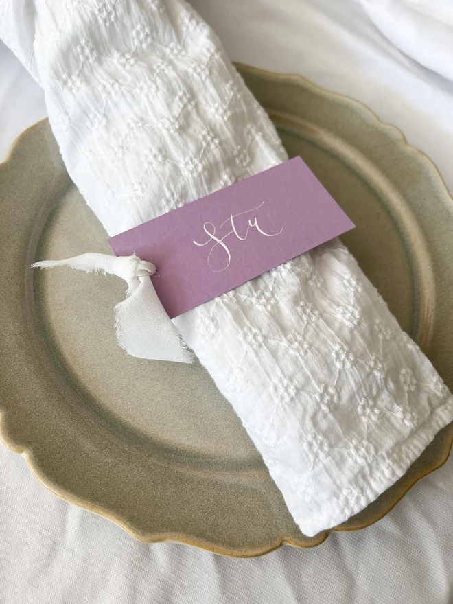 Personalised Calligraphy Wedding Lilac Place Cards, lilac place card written on a white napkin on a plate. 