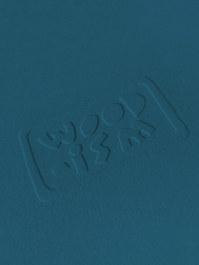 Close up of an embossed Woodism logo on teal paper.