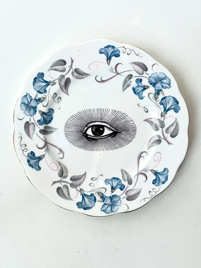 a really ornate blue and white china vintage plate has the vintage black and white image of an eye in the centre