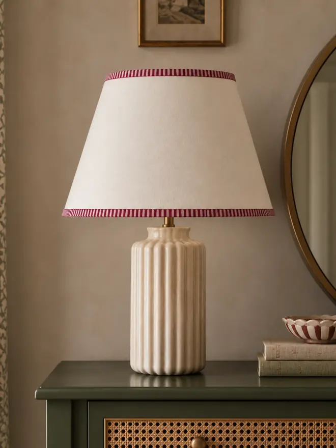 Cream empire lampshade with hand-painted burgundy and pink striped trims, styled on a ribbed ceramic table lamp on a green cane-fronted dressing table