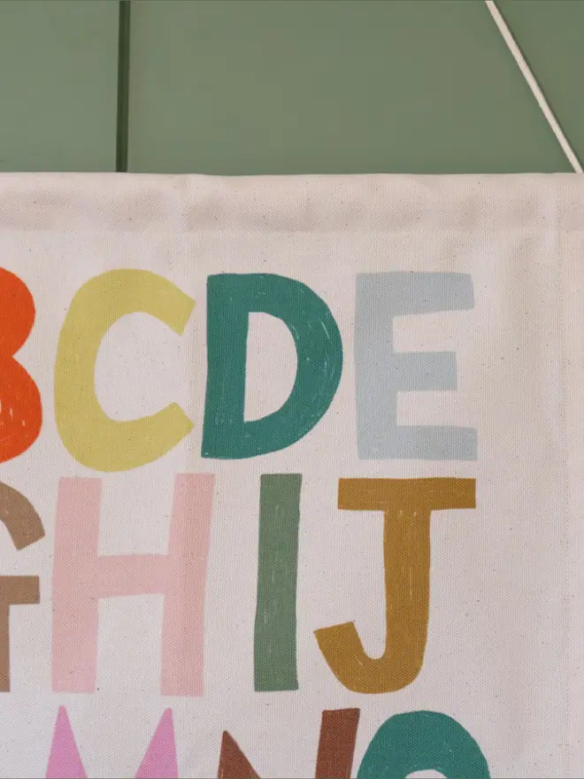Rainbow Alphabet Fabric Banner, hanging on a green wall. 