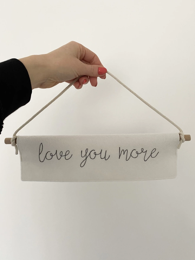 hand holding Love You More Felt Embroidered Banner