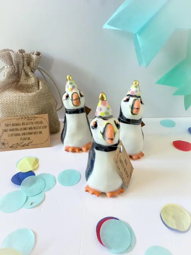 Handmade Porcelain Puffin Penguin Topper With Golden Hat, as a trio grouped on a table near party decorations. 