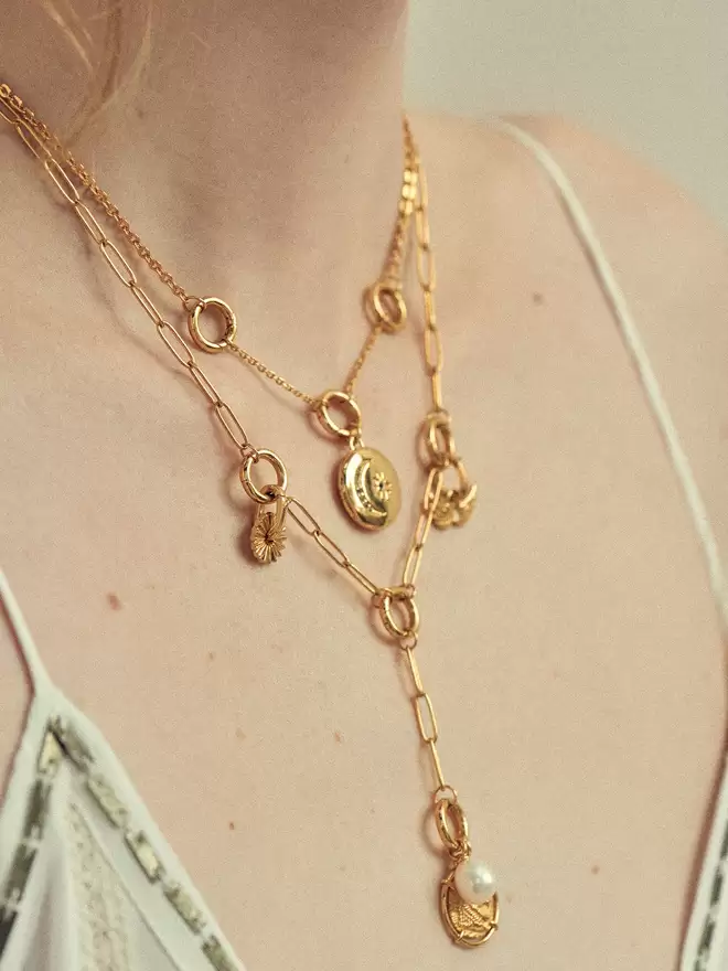 Woman wearing two gold necklaces styled with a gold locket, a lion medallion, a pearl amulet and two gold charms