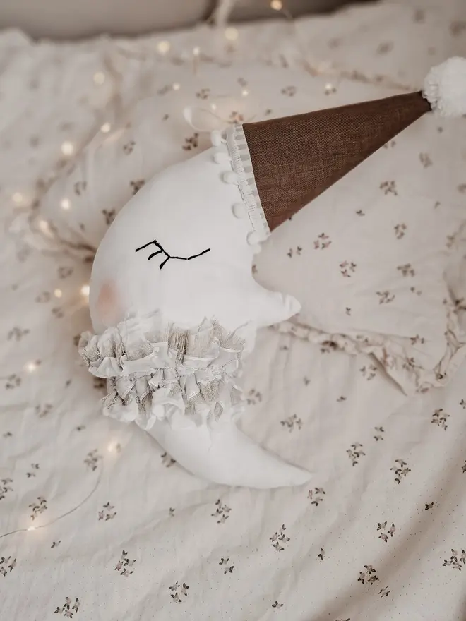 Hanging Moon Pillow Decoration, a hanging moon pillow decoration sitting on a bed surrounded by other bedding accessories. 