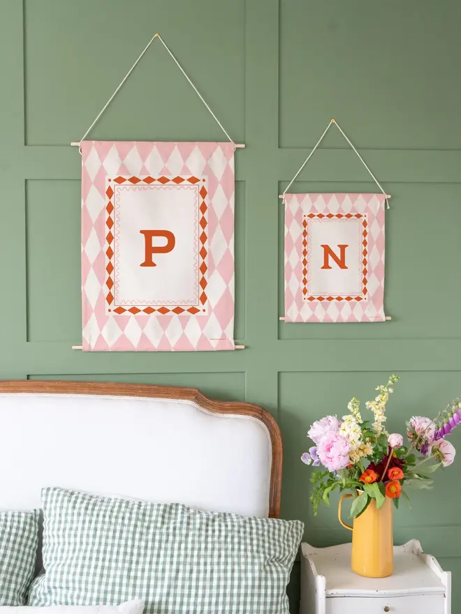Harlequin Initial Fabric Banner, pink mini and midi next to each other against a green wall. 