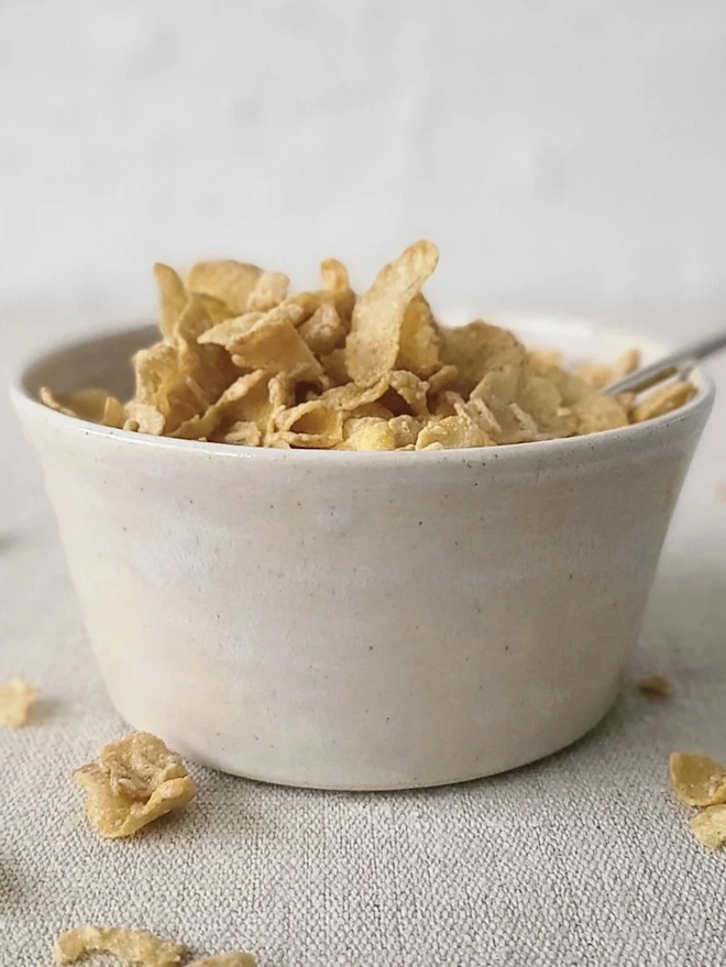 Classic Ceramic Breakfast Bowl, a breakfast bowl sitting on a grey carpet against a plain backdrop. It is accompanied by some cereal and a spoon. 