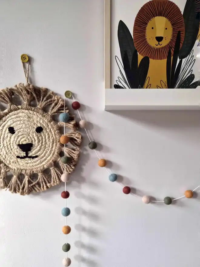 Boho felt ball garland hanging on a wall, with a jungle theme decor in the background.