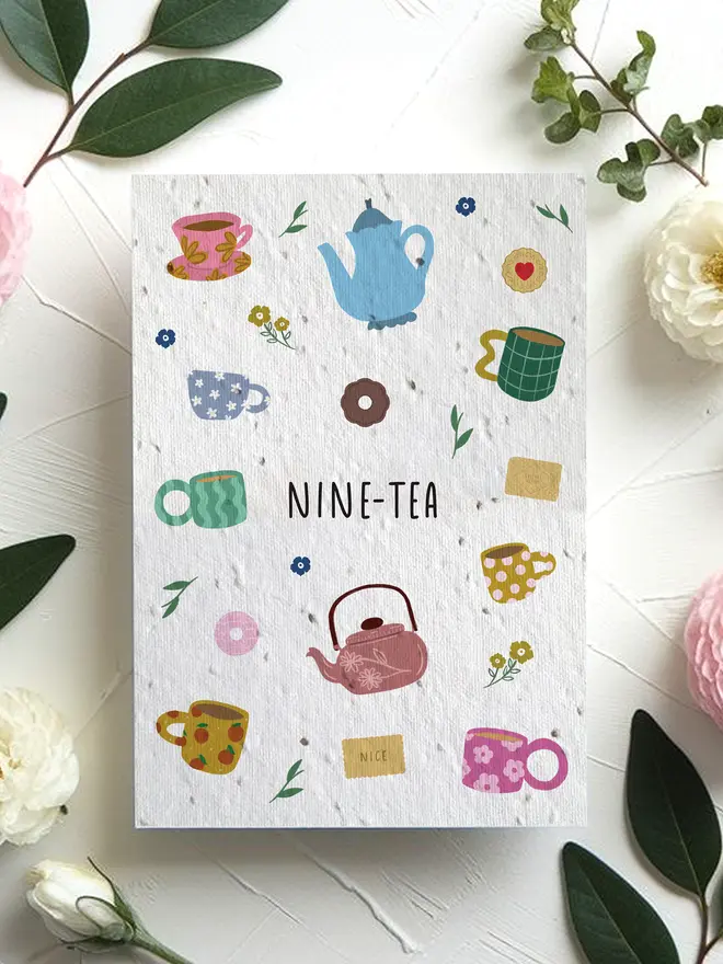 A greeting card titled “NINE-TEA” featuring colorful illustrations of teapots, mugs, tea bags, and small flowers, surrounded by pink and white blossoms with green leaves on a white textured surface.