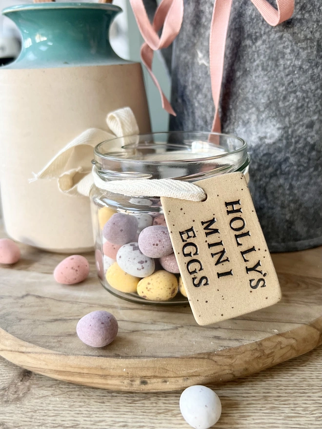 A jar of mini eggs with a neutral ceramic tag attached with cream ribbon, the tag reads ' Holly's Mini Eggs' 