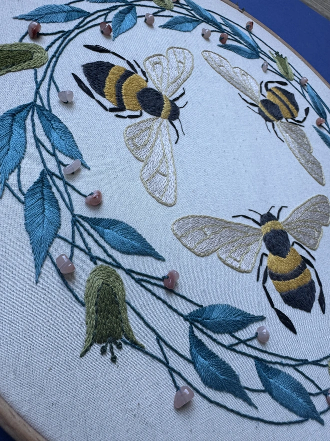 Close up of an embroidery hoop containing hand stitched leaves flowers bees and beads