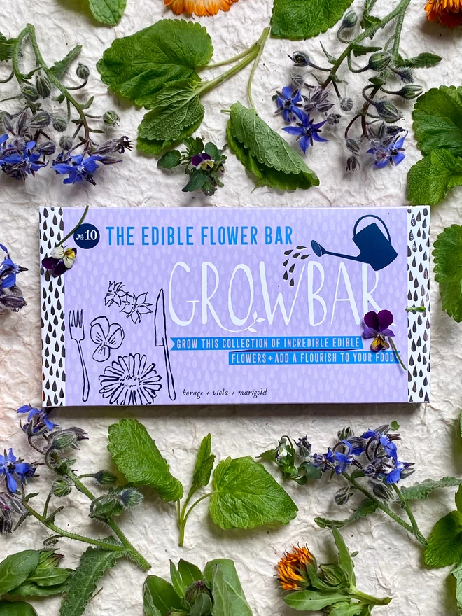 The Edible Flowers Growbar surrounded by blue borage flowers, orange marigold and purple violas. 
