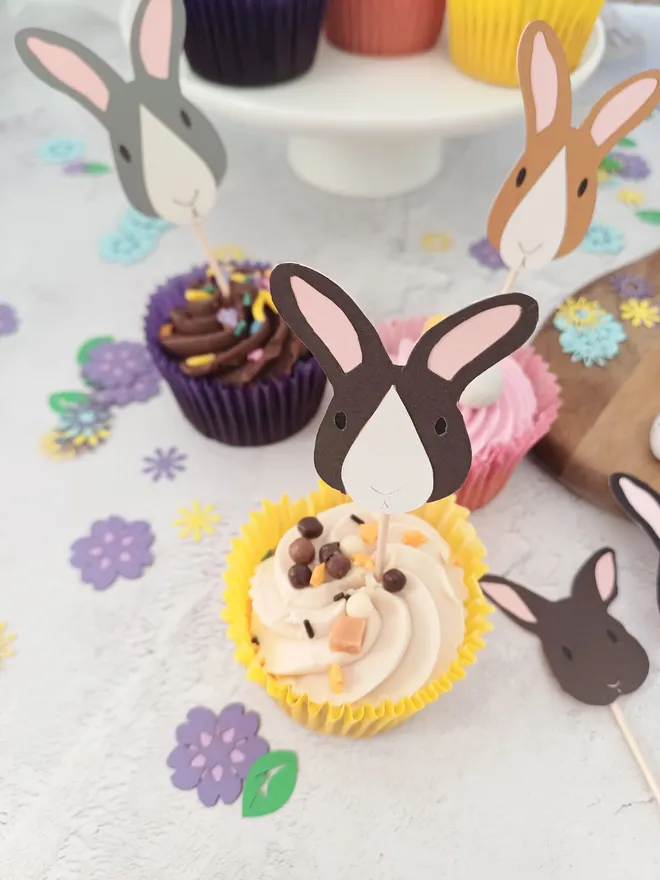 Dark Brown and White, Dark Gray and White, Toffee and White Bunny Cupcake Decorations placed in cupcakes on a table decorated with spring flower confetti