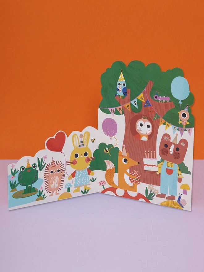 A forest birthday party themed die cut Birthday card filled with colourful and cute characters in party hats such as a fox, bear, owl, frog and rabbit. The card is complete with gold foil details and a gold foil ‘Happy Birthday’ message