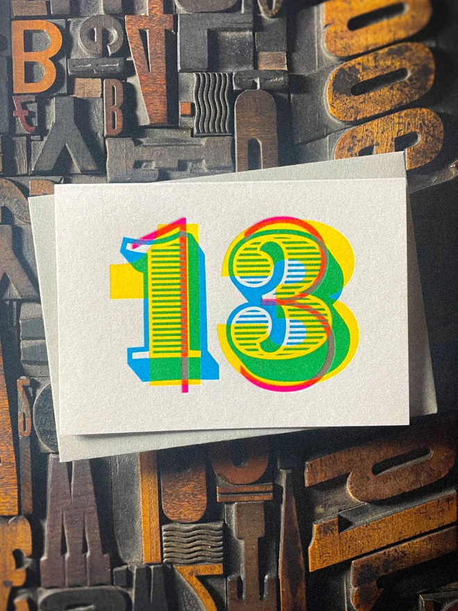 Contemporary handmade 13th birthday letterpress card with a grey Colorplan envelope, featuring bold layered typography printed in cyan, magenta and yellow inks on thick GF Smith Colorplan Pristine White card.