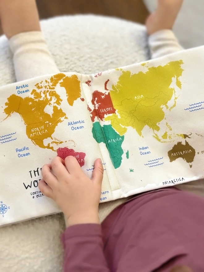 little girl holding the first world atlas soft book and looking at the pages with the world map on it