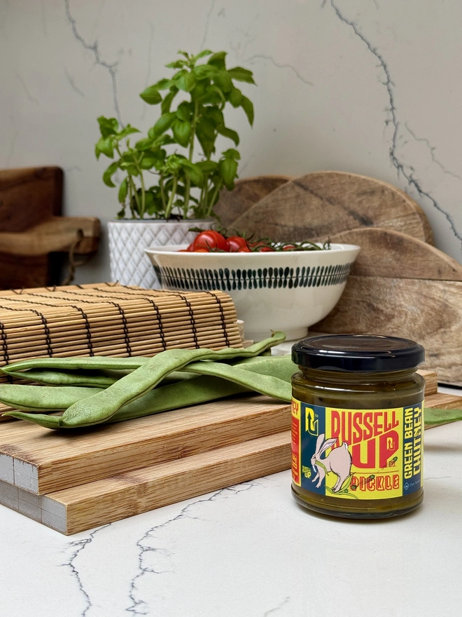 father's day pickles - cheese set. a jar of green bean chutney photographed next to a chopping board green beans.